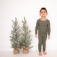 Child wearing green pajamas standing beside two small trees on a white background