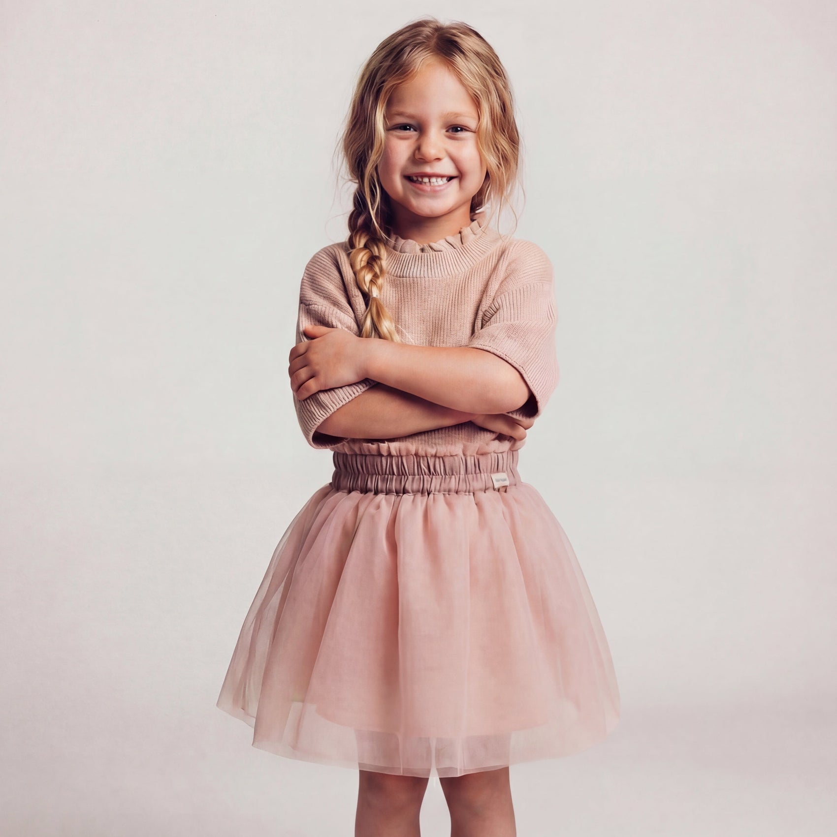 Young girl wearing a pinkish-tan sweater with a tulle pink skirt with a plain background