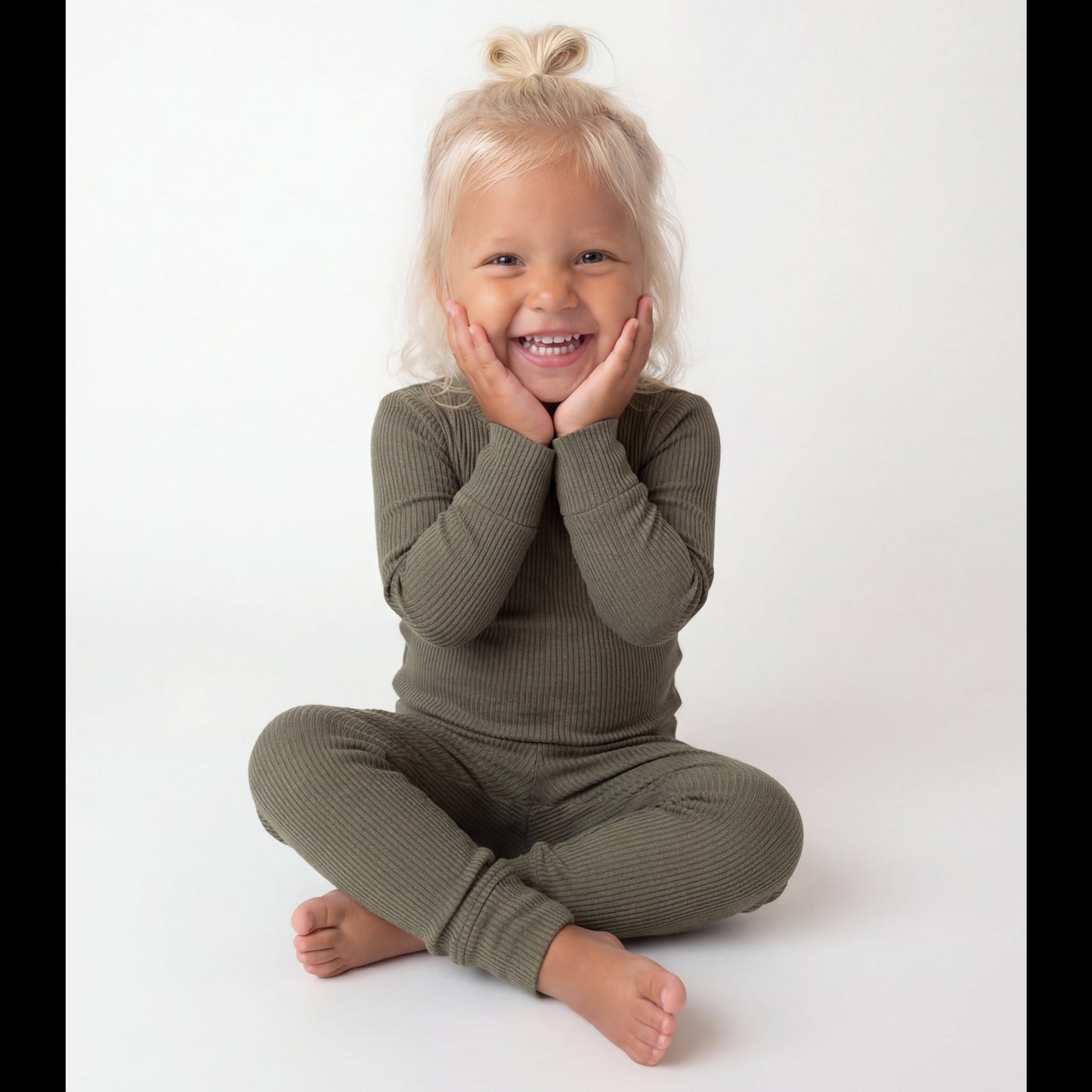 Child wearing a green outfit sitting on a white background